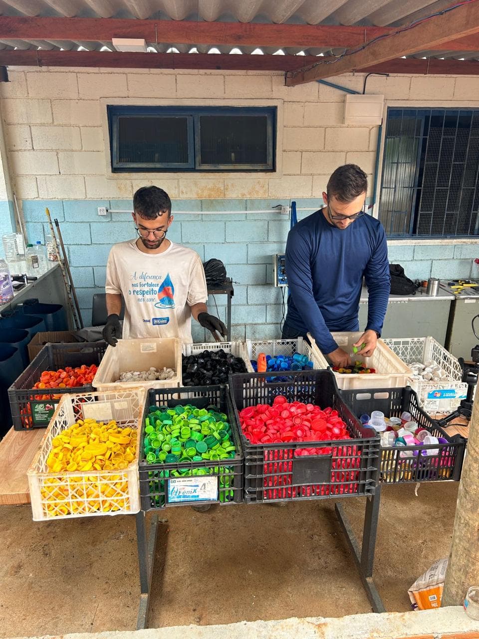Equipe separando tampinhas plásticas por cor em caixas durante a triagem